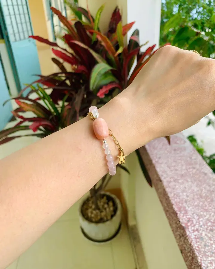 Ảnh khách gửi: cổ tay đeo vòng hạt hồng cam có charm ngôi sao, nền cây xanh