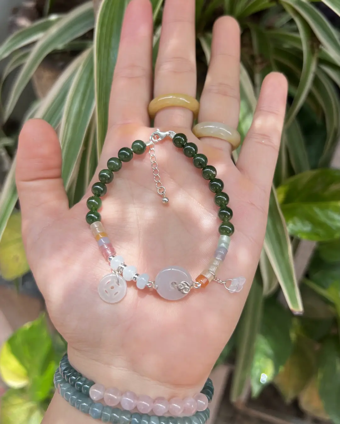 Lòng bàn tay cầm vòng hạt ngọc xanh đậm phối charm ngọc trắng, nền lá cây