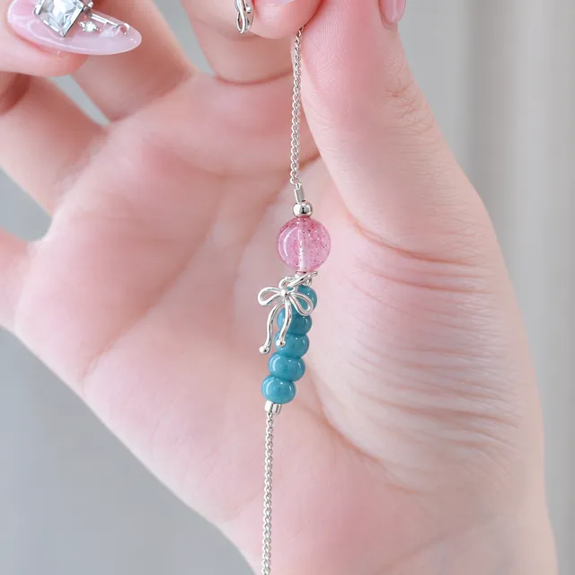 Bàn tay cầm lắc bạc có hạt thạch anh dâu tây hồng, chuỗi hạt xanh ngọc và charm nơ bạc
